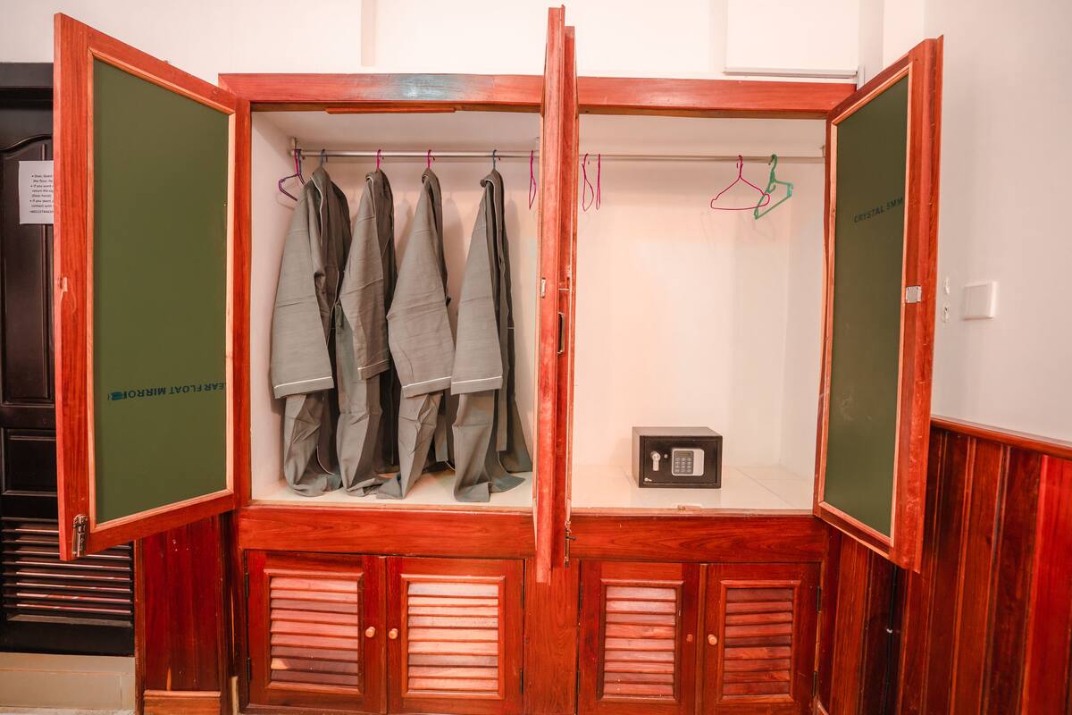 A wooden wardrobe with multiple doors, containing hanging clothes and a small safe.