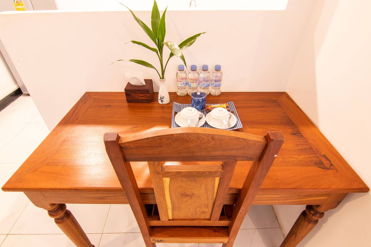A wooden dining table with a vase of green leaves, four water bottles, a tissue box, and two white plates with a checkered napkin.
