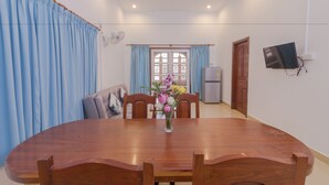 A dining area with a wooden table and chairs, a vase with flowers, and a view of a kitchen and a door. - Aster Villa (Siem Reap)