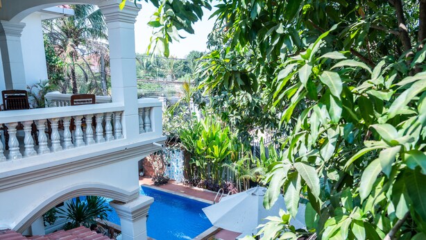 A pool area with a view of a lush garden, white balustrades, and a tiled roof. - Aster Villa (Siem Reap)