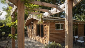 A wooden cabin with a porch, a dining area with chairs, and a gravel pathway. - The elbowroom escape (Donard)