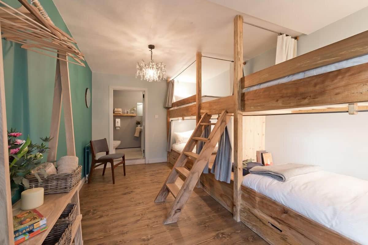 Habitación con literas, una escalera de madera, un candelabro y una estantería con libros y una planta.