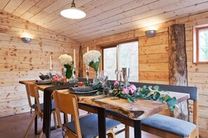 A wooden cabin interior with a dining table set for four, surrounded by chairs, and a large window providing natural light. - The elbowroom escape (Donard)