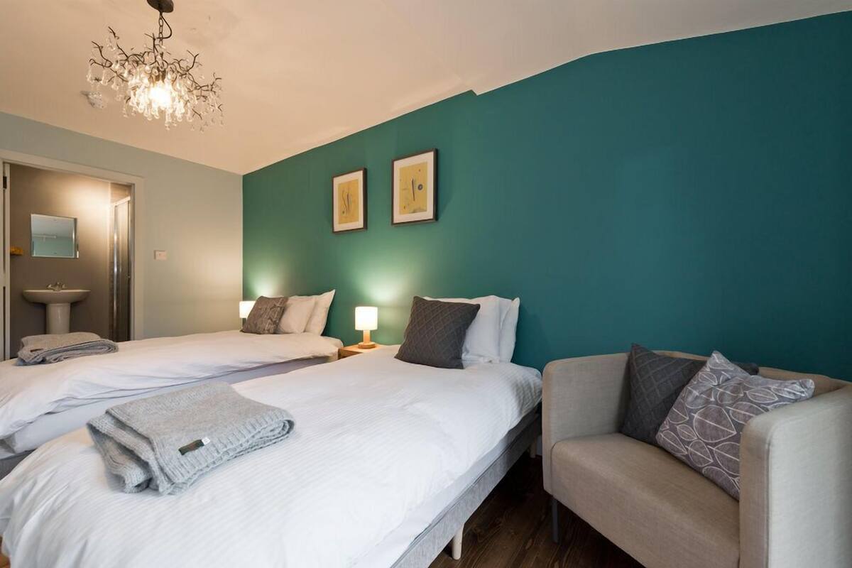 Una habitación de hotel con dos camas, un sofá, una araña de cristal y obras de arte en la pared.