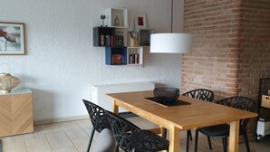 Un comedor con mesa de madera, sillas negras, una lámpara blanca y una estantería con libros y objetos decorativos.