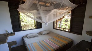 Un dormitorio con cama, dos ventanas, una mesita de noche y una mosquitera.