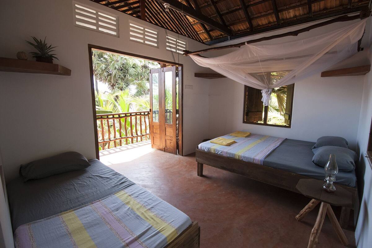 A room with two beds, a small table, and a window with a view of greenery.