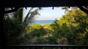 Vista desde un balcón de madera con vista a una playa, palmeras y el océano.