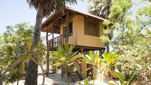 Una estructura de madera de dos pisos con un balcón, rodeada de vegetación tropical.