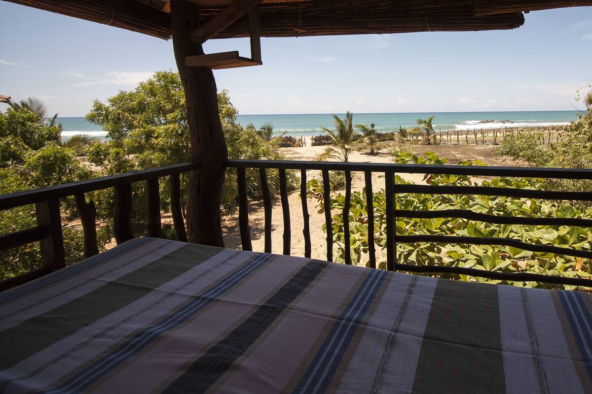 A balcony with a striped tablecloth overlooking a beach with palm trees and the ocean.