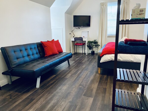 A modern room with a black sofa, a bed, a desk, a TV, and a window with curtains. - The Loft (East Maitland)