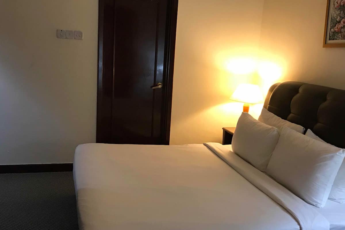 A hotel room with a bed, a nightstand with a lamp, a door, and a wall socket.
