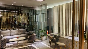 A modern lobby with a sofa, coffee table, and chairs. There is a reception desk with a plant and a fire extinguisher. - Times Square Service Suites (Kuala Lumpur)
