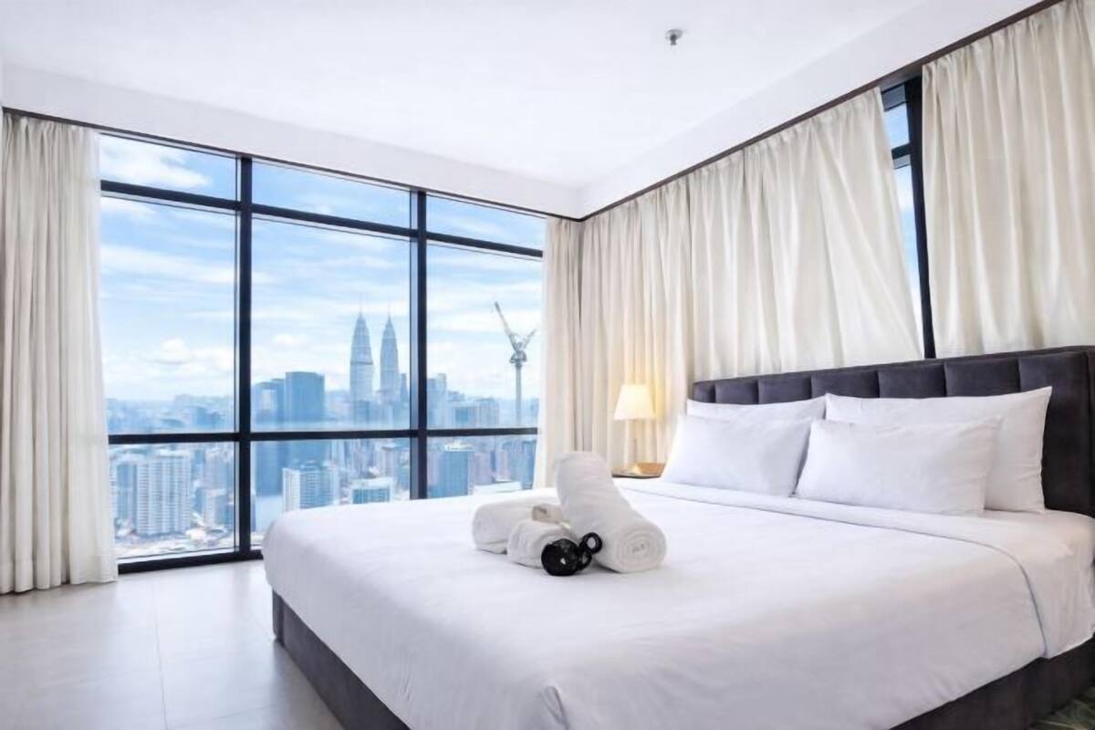 A hotel room with a large bed, a view of a cityscape, and a window with curtains.