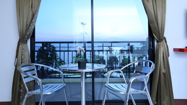 A balcony with a table and two chairs, overlooking a scenic view of the ocean and palm trees. - Sunlight Hotel (Pattaya)