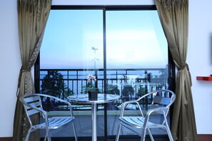 A balcony with a table and two chairs, overlooking a scenic view of the ocean and palm trees. - Sunlight Hotel (Pattaya)
