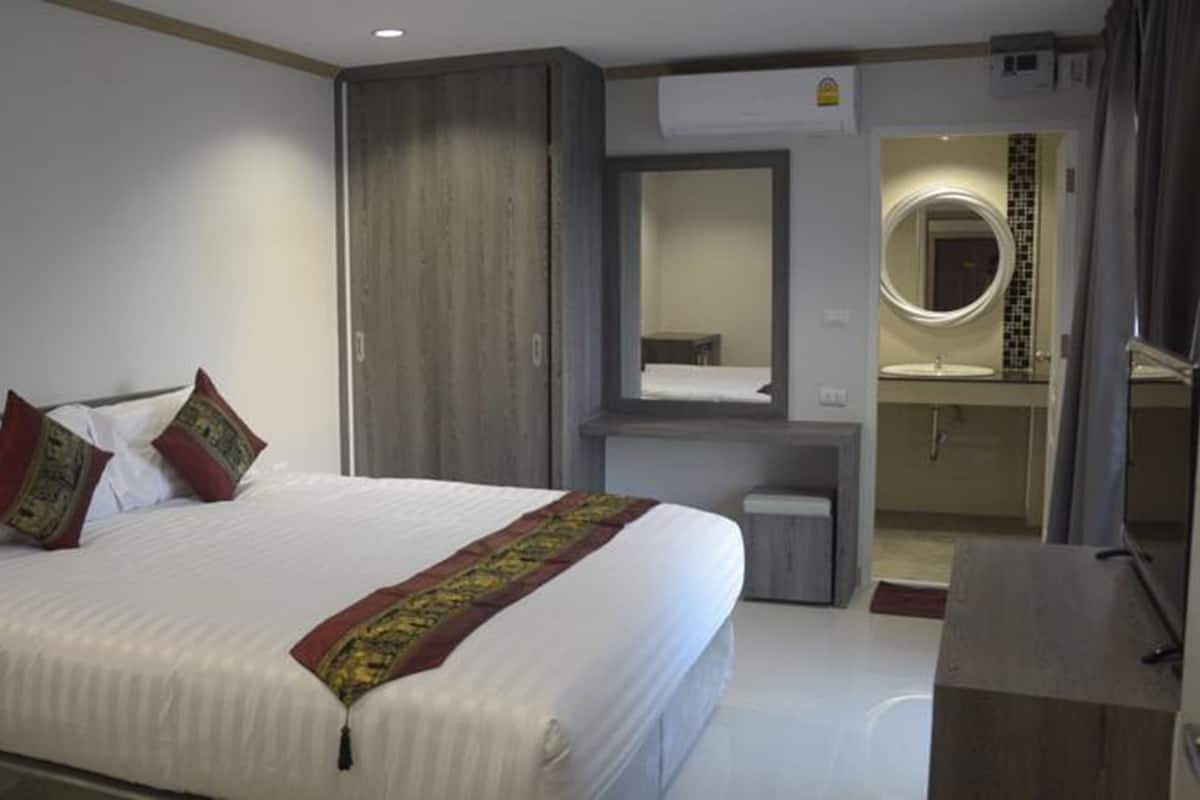 Une chambre d’hôtel avec un grand lit, une armoire, un miroir et une salle de bain équipée d’un lavabo et d’un miroir.