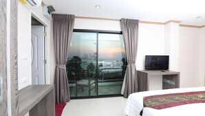 A hotel room with a bed, a TV on a wooden stand, a balcony with curtains, and a view of the sunset. - Sunlight Hotel (Pattaya)