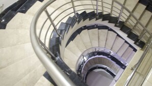 Uma escadaria em espiral com corrimão de metal e degraus bege.