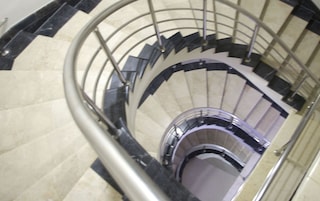 Uma escadaria em espiral com corrimão de metal e degraus bege.