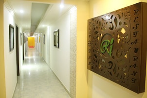 A hotel corridor with framed pictures on the walls, a decorative metal wall art piece with the letters "R", "J", "T", "A", "N", "T", "E", "S", "T", "A", "R", "E", "N", "T", "E", "R", "S", "T", "A", "R", "E", "N", "T", "E", "R", "S", "T", "A", "N", "T", "E", "R", "S", "T", "A", "N", "T", "E", "R", "S", "T", "A", "N", "T", "E", "R", "S", "T", "A", "N", "T", "E", "R", "S", "T", "A", "N", "T", "E", "