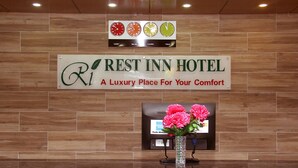 Placa do Hotel Rest Inn com um relógio acima e um vaso com flores abaixo.
