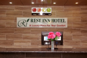 Placa do Hotel Rest Inn com um relógio acima e um vaso com flores abaixo.