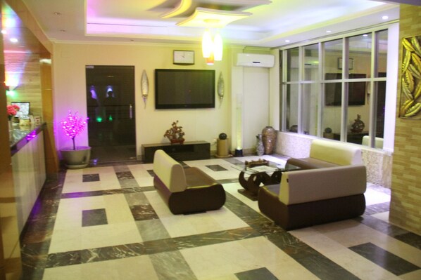 Un hall de hotel con piso a cuadros, un sofá, una mesa de centro y un televisor en la pared.