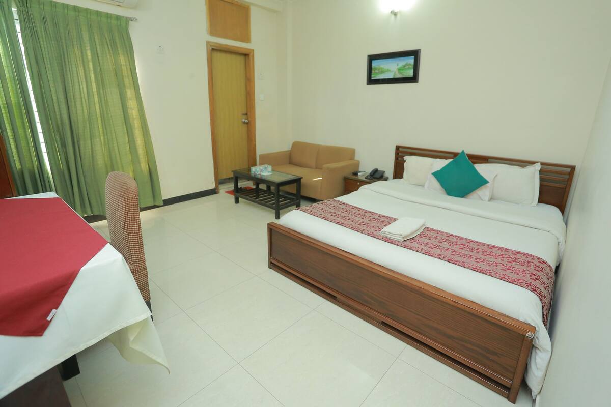 Une chambre d’hôtel avec un lit, une chaise, une petite table et un bureau recouvert d’une nappe rouge.