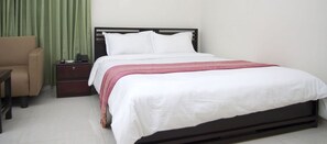 A neatly made bed with white linens and a pink patterned throw, a wooden nightstand with a telephone, and a green curtain. - Restinn Hotel & Restaurant (Moulvibazar Sadar)