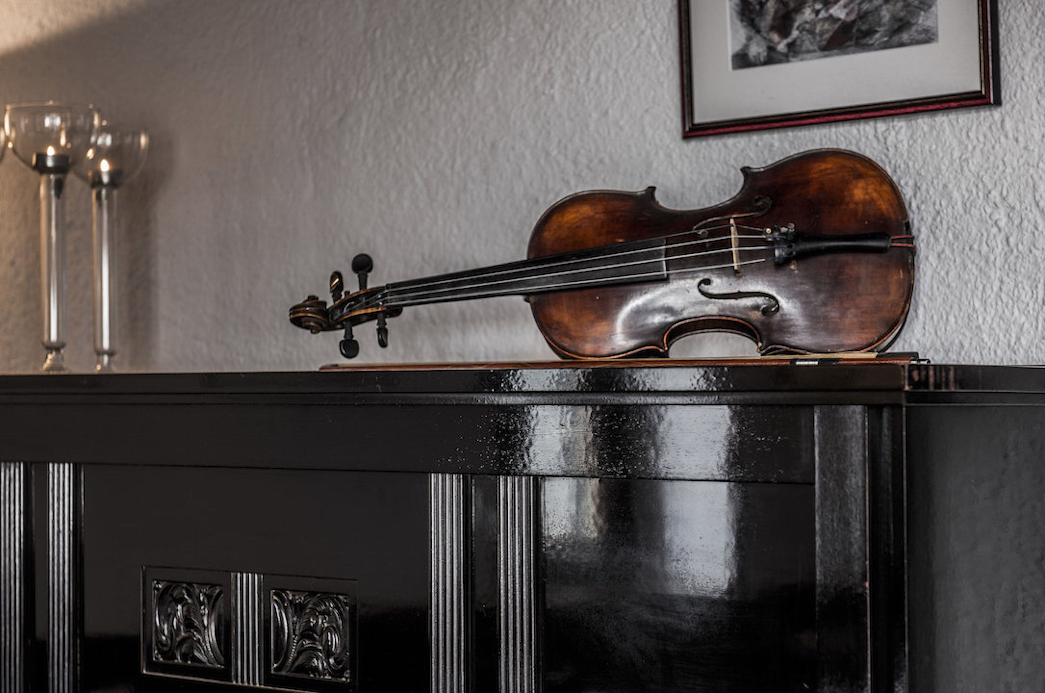 Un violon posé sur un meuble noir, avec un tableau encadré accroché au mur derrière.