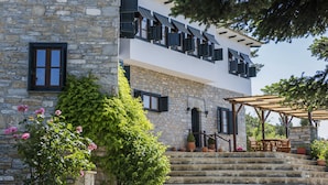 A two-story stone building with a stone staircase leading to a wooden deck with outdoor furniture. - Arxontiko Mytilineou Skretaion (South Pelion)