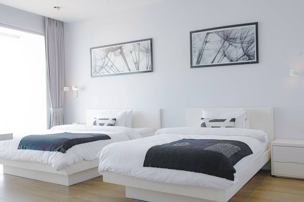 A modern bedroom with two beds, white bedding, and abstract wall art.