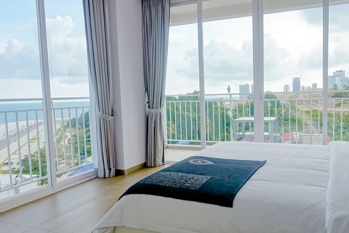 A hotel room with a large bed, a view of the city, and a balcony with a railing.