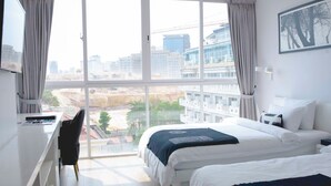 A hotel room with two beds, a desk, and a large window offering a view of the cityscape and construction site. - La Vogue Boutique Hotel & Casino (Sihanoukville)