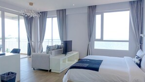 A modern hotel room with a bed, a TV on a white console, a seating area with a chair, and large windows offering a view of the sea. - La Vogue Boutique Hotel & Casino (Sihanoukville)