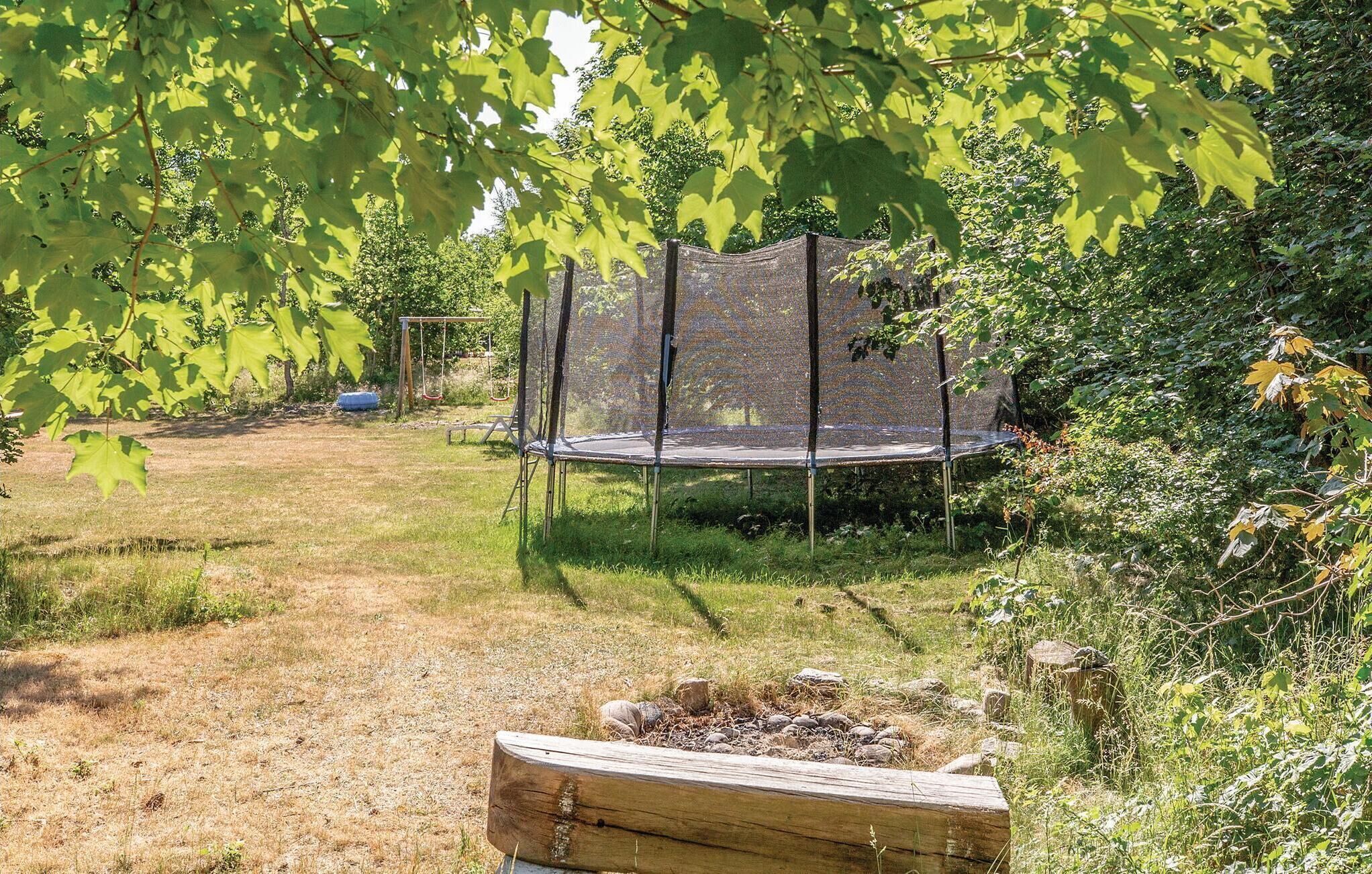 A trampoline surrounded by a wooden fence in a grassy area with trees.