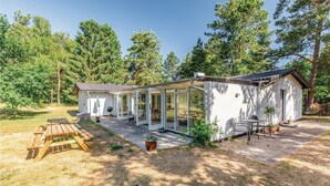 Una casa pequeña y blanca de un piso con un patio, una mesa de madera y sillas.
