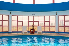 An indoor swimming pool with a view of a city skyline through large windows. - Palette Luxury Marina View Formerly Happy Days Hotel (Manama)