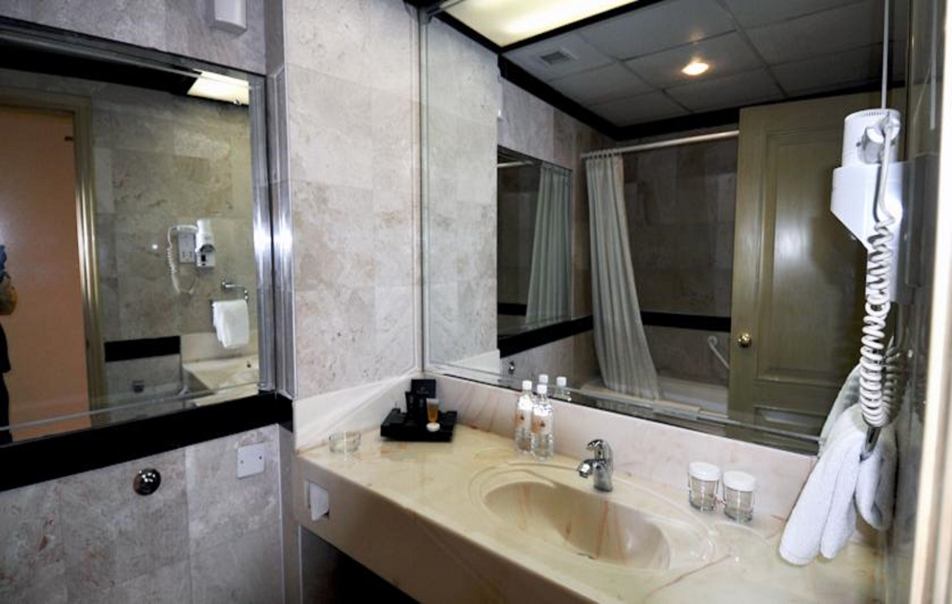 Un baño de hotel con un espejo grande, un lavabo, un teléfono y una zona de ducha.