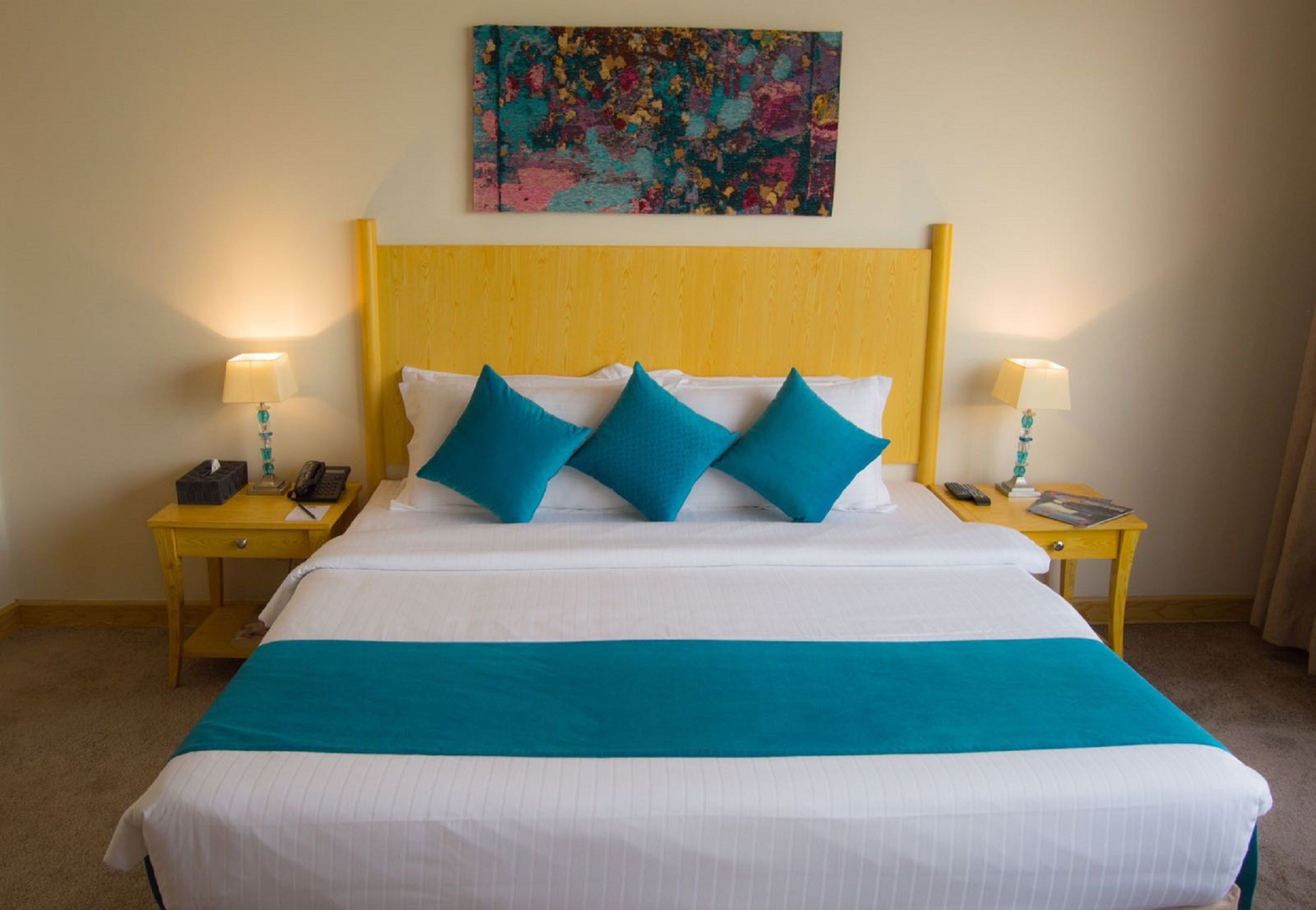 A neatly made bed with a teal bedspread and pillows, two bedside tables with lamps, a phone, and a magazine.