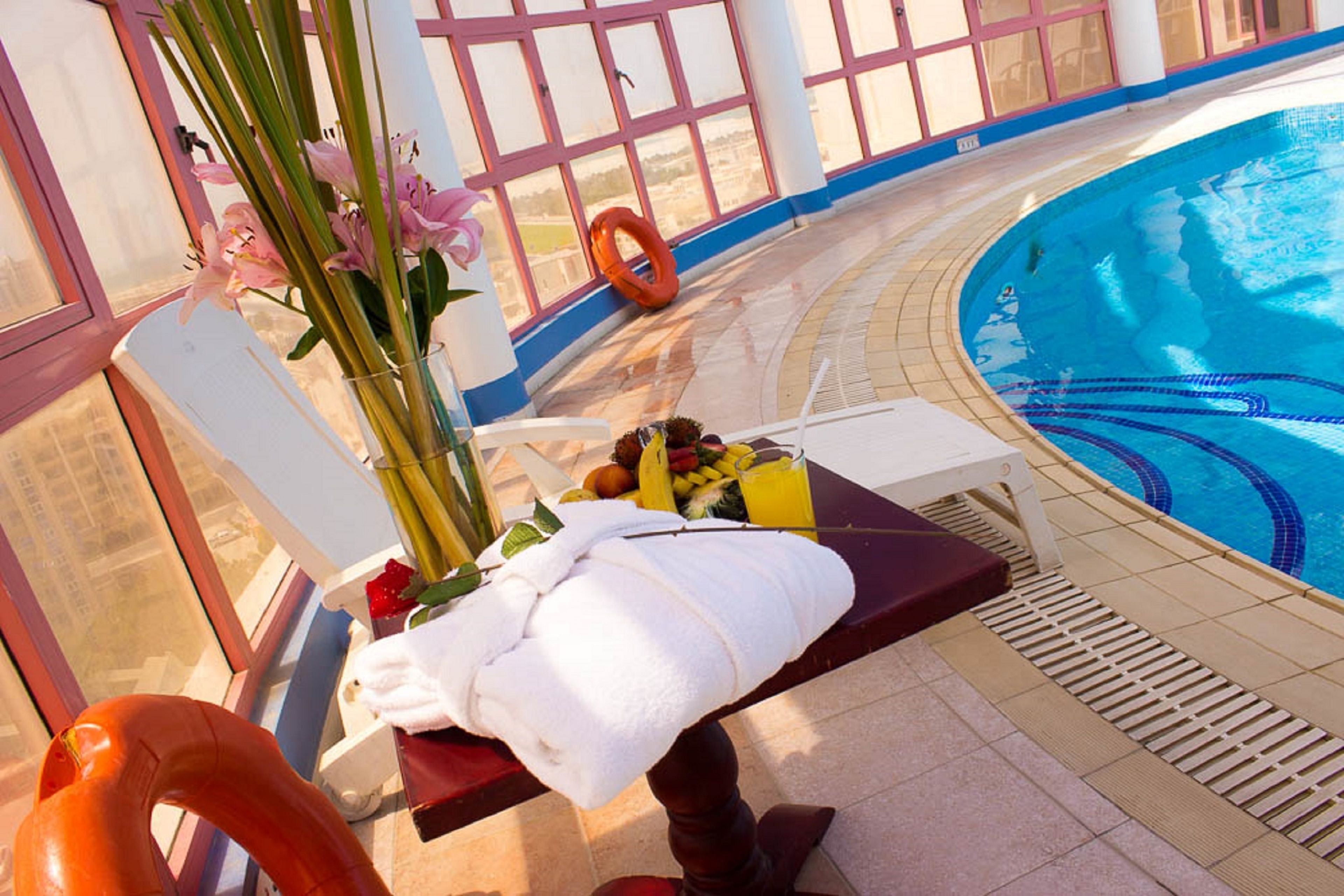 A poolside area with a lounge chair, a towel, a fruit basket, and a vase of flowers.