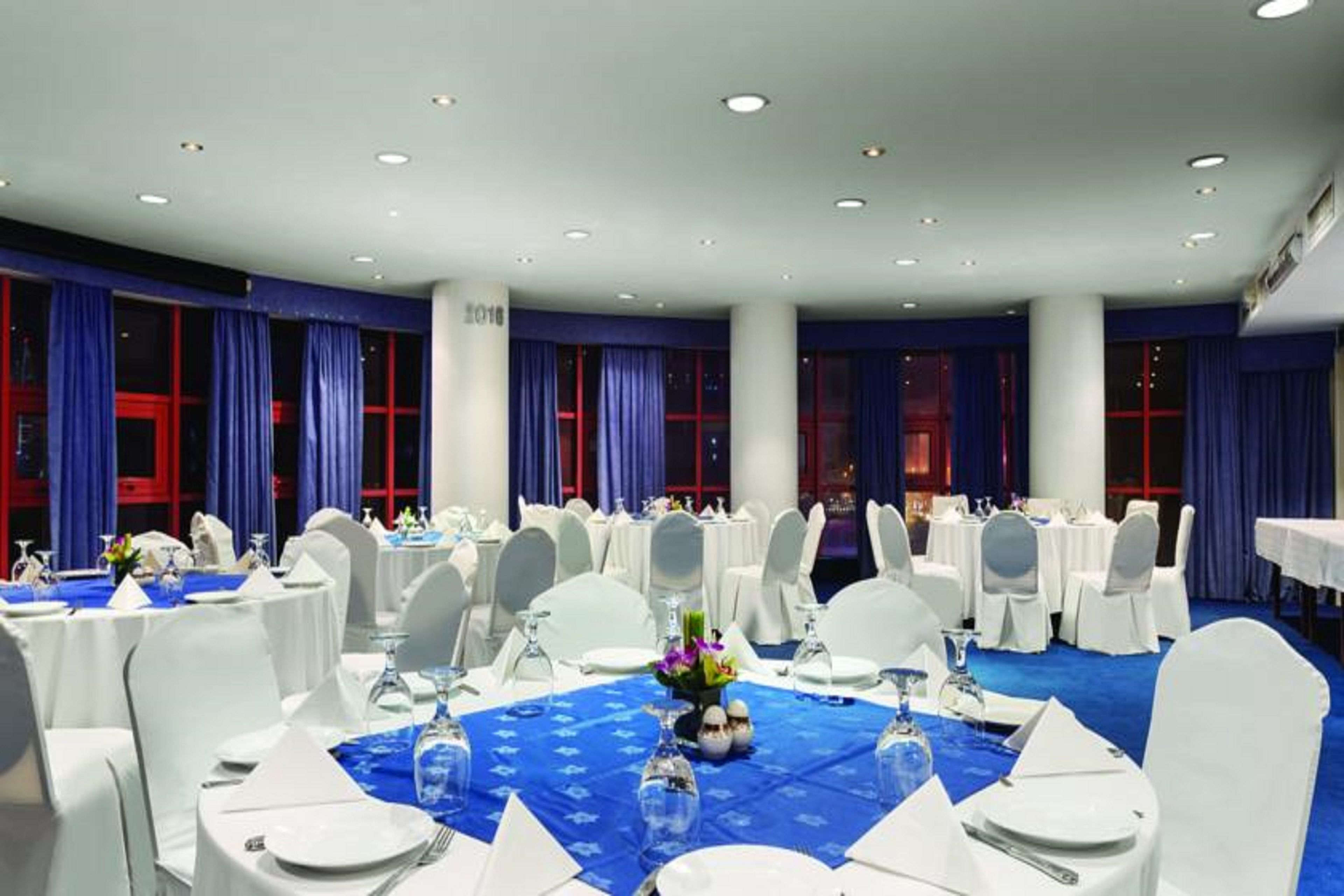 A banquet hall with round tables set for dining, white chairs, and blue tablecloths.