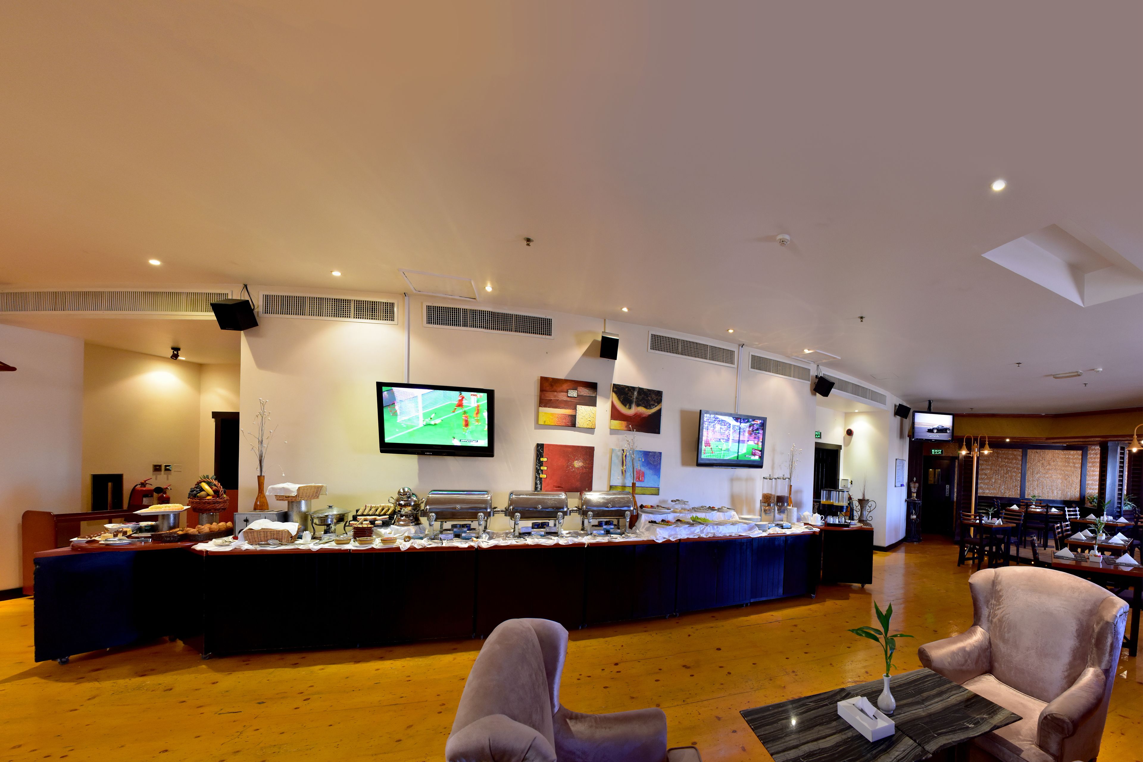 A hotel lobby with a buffet, seating area, and multiple screens displaying sports.