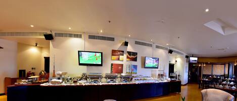 A hotel lobby with a buffet, seating area, and multiple screens displaying sports.