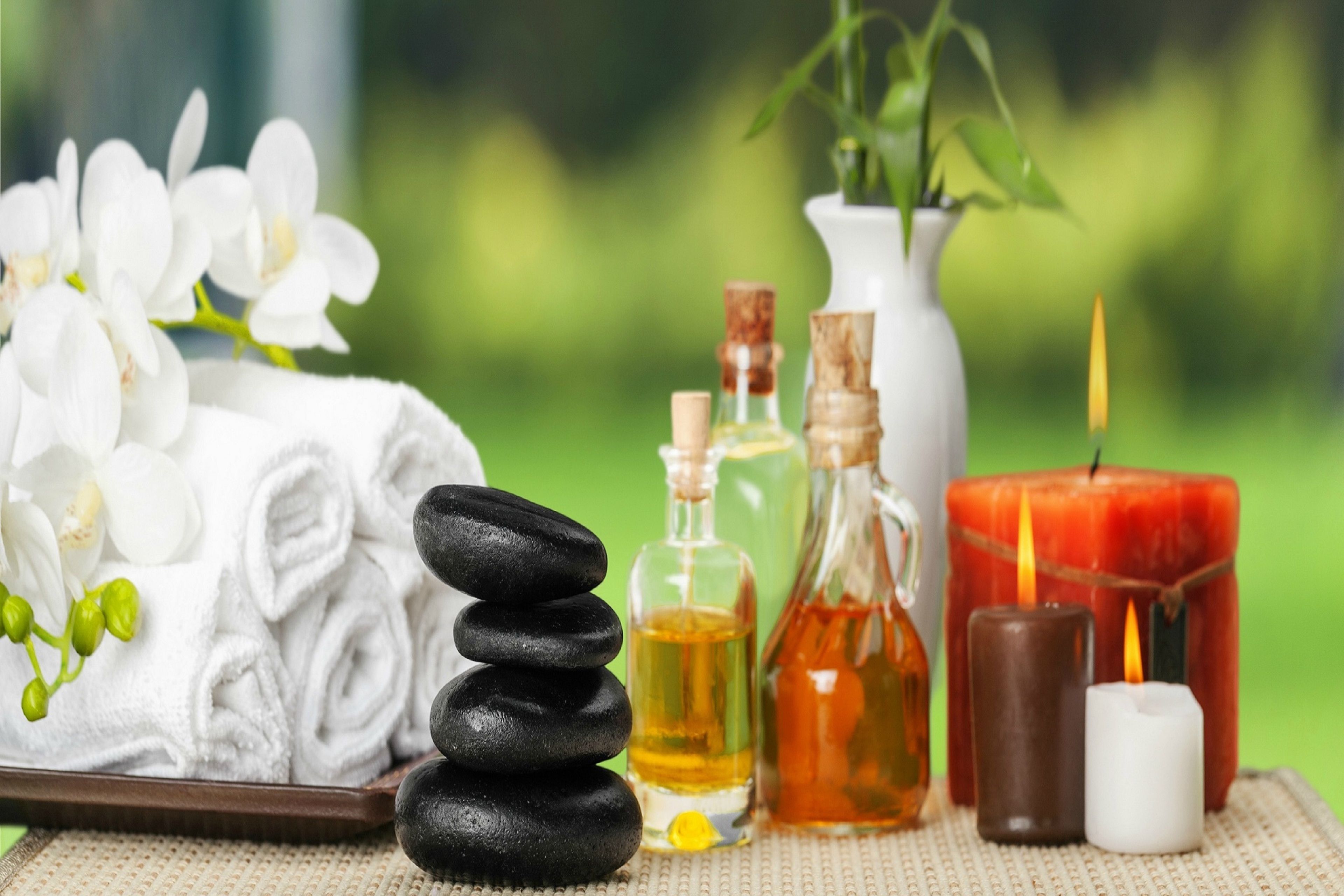 A spa setting with a stack of black stones, white towels, a white candle, and two candles in a jar and a glass bottle.