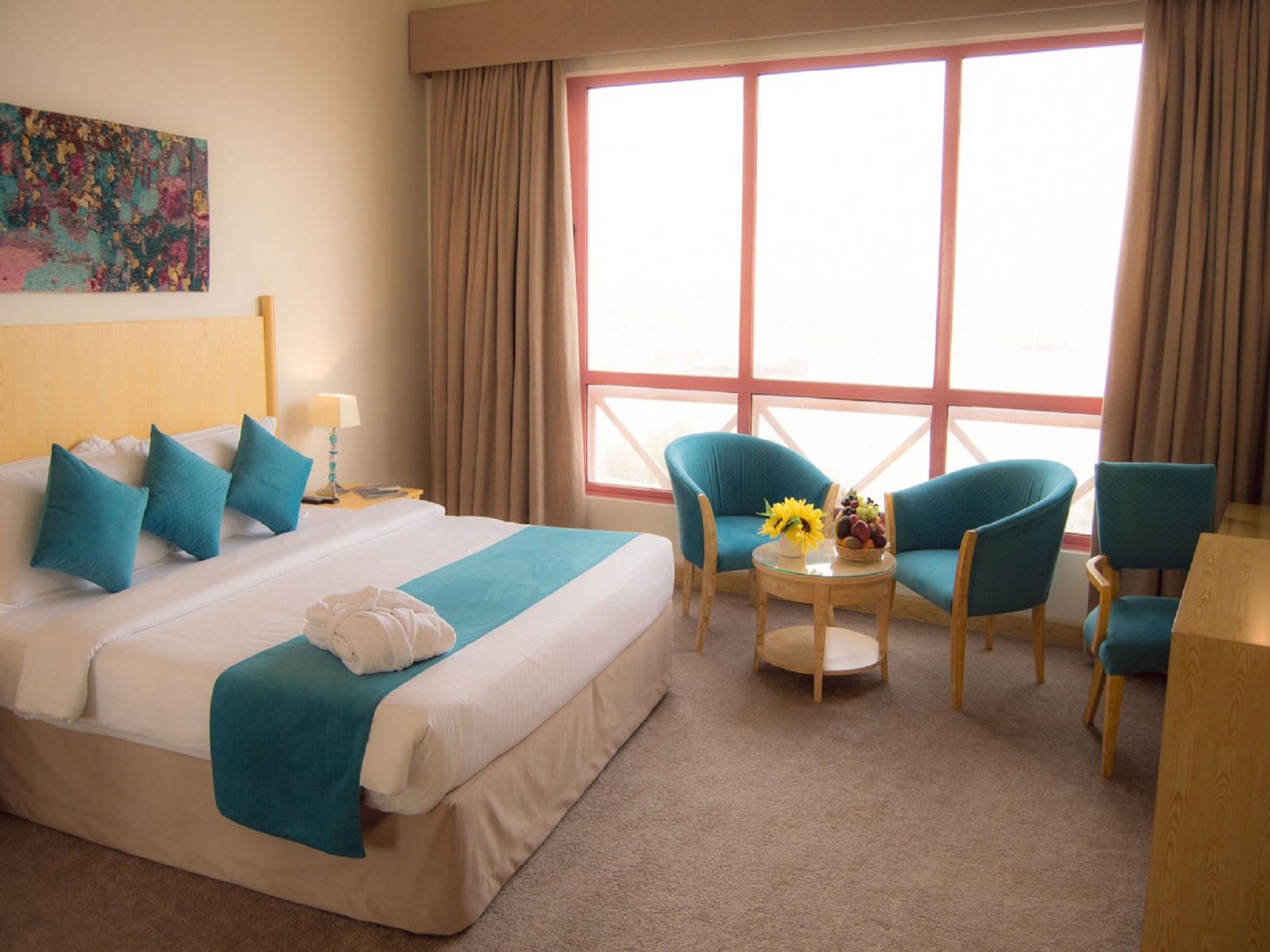 A hotel room with a large bed, two chairs, a small table with a vase of flowers, and a window with curtains.