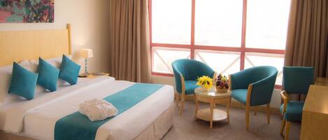 Una habitación de hotel con una cama grande, dos sillas, una mesita con un jarrón de flores y una ventana con cortinas.
