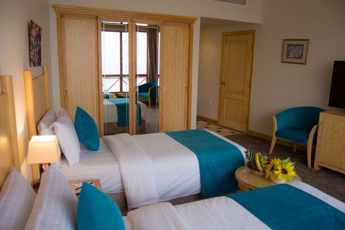 Ein Hotelzimmer mit zwei Betten, einem Kleiderschrank, einem Fernseher und Blick auf einen Balkon.