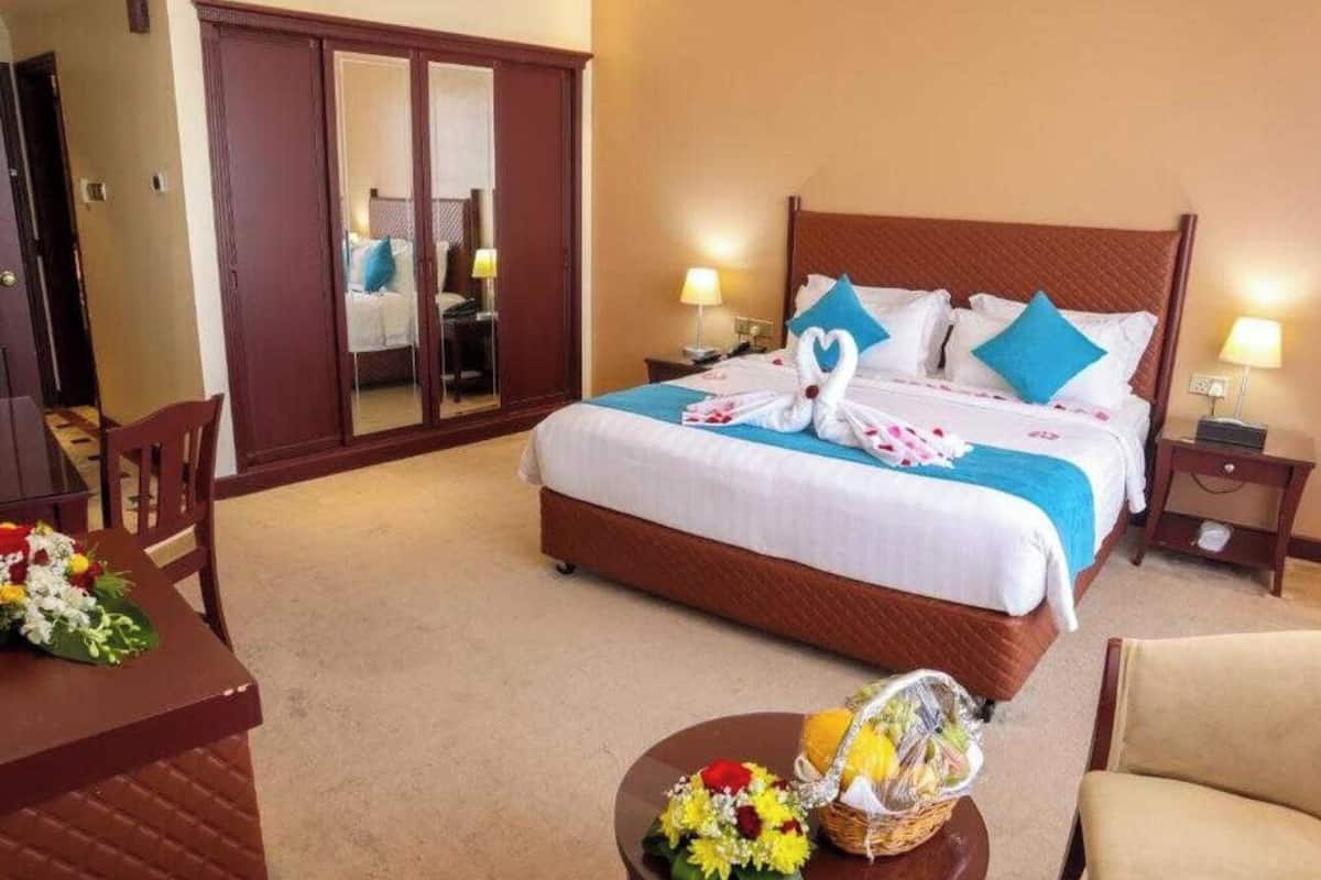 Ein Hotelzimmer mit einem großen Bett, einem Holzschrank, einem Schreibtisch mit Stuhl und einem kleinen Tisch mit Blumen.